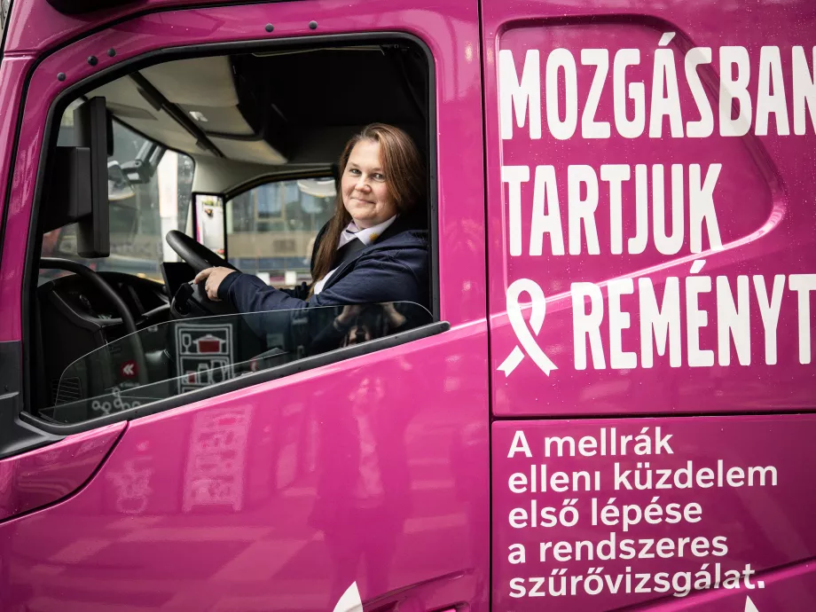 Női sofőr vezet egy rózsaszín kamiont a magyar utakon